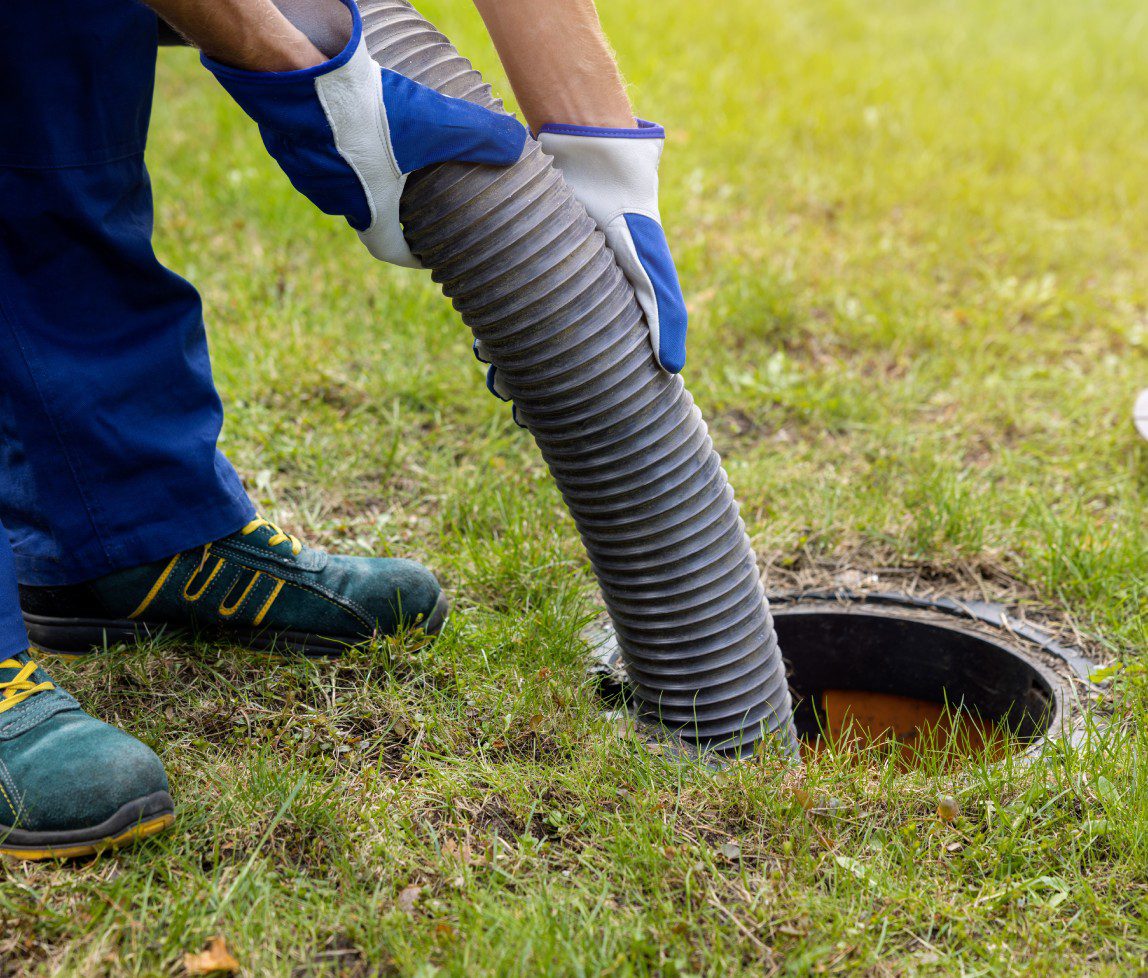 Person inserting a flexible pipe into a ground drain outdoors.
