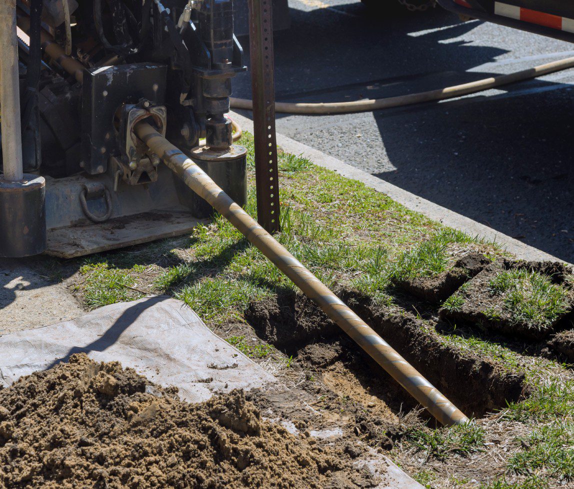 Heavy machinery digging a trench next to a road with soil piled nearby.